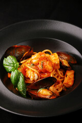 pasta with seafood closeup with black plate on dark background. Italian spaghetti pasta marinara with Mussels, shrimp and tomatoes