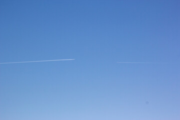 Two planes fly towards each other. Inversion trail of clouds from the plane against the blue sky. Airplane leaving vapor trail behind. Track in the sky from a jet plane.