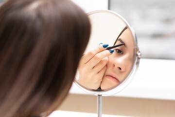 Teen girl applies makeup looking in the mirror, paints her eyebrows with a pencil