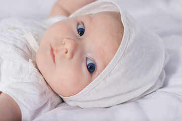 Little baby girl with blue eyes in white dress and hat on white blanket