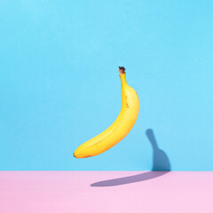 Levitating banana against vibrant pastel blue and pink background. Minimal trendy food concept.