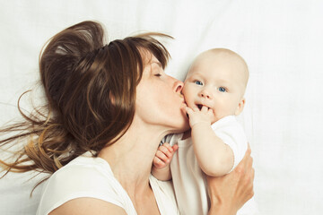 Young mother plays with her baby on a bed with a white sheet. Flat lay, top view