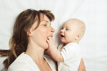 Young mother plays with her baby on a bed with a white sheet. Flat lay, top view