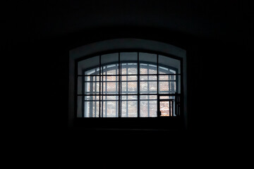 A window in a prison cell, covered with bars. The interior of an old dark solitary prison cell.