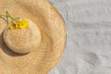 Fototapeta na wymiar Flat lay composition with stylish straw hat and three yellow flowers on sand.