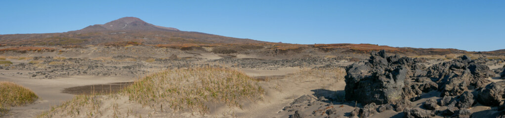 Panoramic view of the mountains on the way to the Mutnovsky volcano. Autumn view of the volcano and igneous stones after a volcanic eruption against the blue sky. Kamchatka Peninsula, Russia.