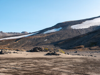 Volcanic rock road to Mutnovsky volcano. View of the mountains covered with volcanic dust and snow...