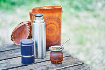 Mate Kit Lined in Leather, with the light bulb, thermos and bag on a wooden table in the countryside