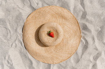 Fototapeta na wymiar Top view of a ripe strawberry on a straw hat on the sand.