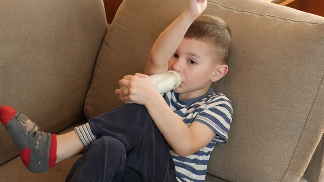 Little boy eats porridge cooked in a bottle.