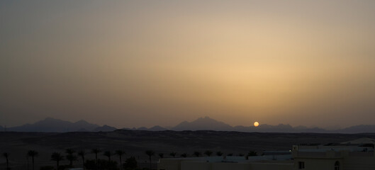The sun sets behind the mountains against the backdrop of a sandy desert. Egypt.