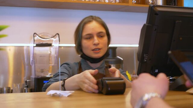 A girl cashier in uniform enters data on the monitor screen and gives a terminal for payment to the visitor, he pays uses the NSF payment. Cashir thanks for your purchase. Small business. Close-up.