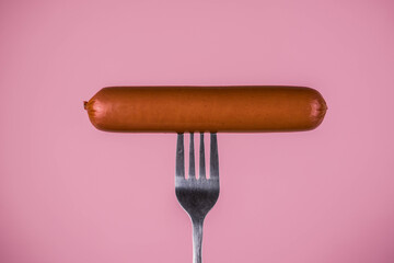 Sausage on a fork on a pink background