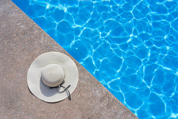 Fototapeta na wymiar A small elegant hat lies near the pool in summer while on vacation