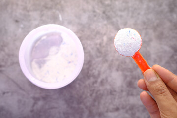 Washing powder in plastic spoon on black background top view.