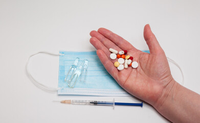 hand with syringe and medical mask and capsules on white background