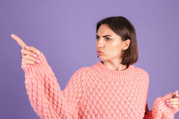 Young brunette isolated on purple background shouts angrily, reproachfully accuses someone, points...