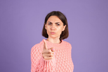 Young brunette in sweater isolated on purple background shouts angrily, reproachfully accuses you,...