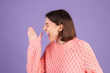 Young brunette in pink sweater isolated on purple background shouting and screaming loud to side with hand on mouth. communication concept.