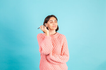 Young brunette in pink sweater isolated on blue background with makeup on face hold blush brush...