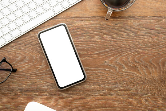 Smartphone with blank mockup screen is on top of wood office desk table with supplies. Top view with copy space, flat lay.