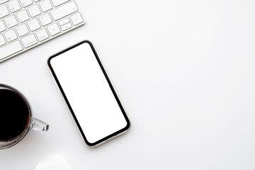 White office desk table with smartphone with blank mockup screen, cup of coffee and computer keyboard. Top view with copy space, flat lay.