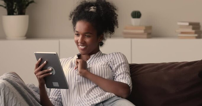 Happy dreamy young african biracial woman web surfing information on digital computer tablet, planning vacation trip travel, purchasing tickets or booking hotel, visualizing future alone at home.