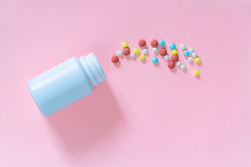 Multicolored tablets, pills, capsules in plastic bottle on pink background, copy space. Medicine, vitamin and nutritional supplements concept.