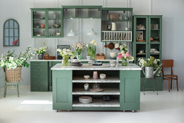 Green kitchen interior with furniture. Stylish cuisine with flowers in vase. Wooden kitchen in spring decor. Cozy home decor. Kitchen utensils, dishes and plate on table. kitchen island in dining room - obrazy, fototapety, plakaty