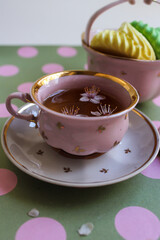 A vintage pink cup of black tea standing on a green background with polka dots. Vintage vase with meringues of yellow and green colors