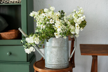 Vintage rustic garden Tool. Daisies in zinc metal vase. Beautiful bouquet of bright flowers in watering can on wooden chair. Bunch of daisies in watering can. Gardening concept. Mother's day.	