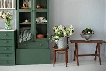 Cozy home decor. Kitchen interior with furniture. Beautiful bouquet of flowers in watering can on wooden chair by cupboard. Gardening concept. Vintage garden Tool. Stylish cuisine with flowers in vase