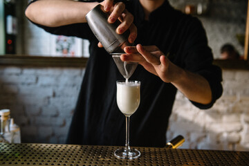 Bartender pouring gin sour cocktail into glass.
