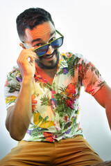 Retrato de hombre joven con barba y lentes de sol y camisa tropical sonriendo con un fondo blanco