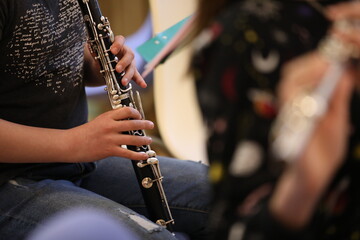 A young hand of a student musician presses the valves of a black clarinet musical instrument with...