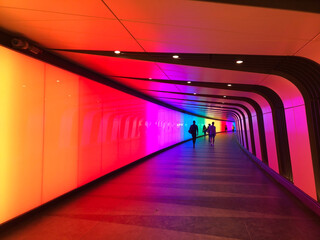Colourful pedestrian tunnel. You can see shapes of people far away at the other end of the tunnel.