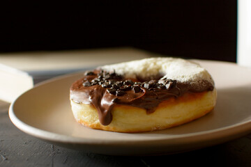 Large donut, dulce de leche, covered with granulate chocolate and powdered milk, on a plate, in close-up, and with a black background