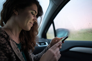 Fototapeta na wymiar Casual young woman waiting inside car while raining and using phone