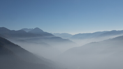 Naklejka na ściany i meble A panoramic view of layers of mountains with fog in the valley and clear blue sky