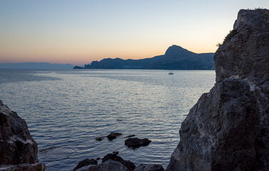 Rocky coast and a pleasure boat with tourists in the sea on a warm summer evening