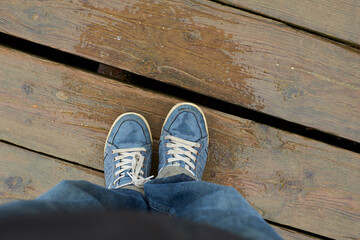 View from above of feet wet from the rain with some sneakers on a wooden floor.