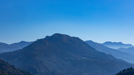 A panoramic view of silhouette of   layers of mountains with fog in the valley and clear blue sky