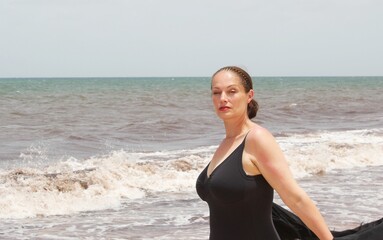 plus size curve model on beach in swimsuit and kimono with sand and waves behind