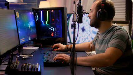 Pro gamer move the buttons on professional mixer late at night in streaming home studio. Streamer playing space shooter video games tournament using RGB keyboard in room with neon lights.