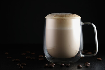Cappuccino in a transparent cup. Cappuccino, glass cup with double walls on a black background. Italian latte macchiato on a black background. Latte macchiato, coffee beans on black.