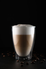 Italian latte macchiato on a black background. Cappuccino, glass cup with double walls on a black background. Cappuccino in a transparent cup. Latte macchiato, coffee beans on black.