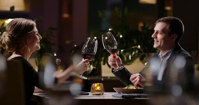 Joyful couple having a romantic dinner at a fancy restaurant. People celebrating their relationship anniversary, saying a toast and drinking wine 4k footage