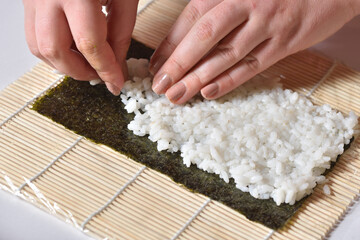 Female hands prepare homemade sushi roll and lay rice on nori leaf.
