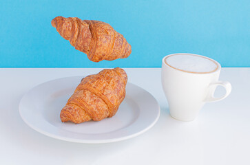 Levitating food. Flying croissants for breakfast and a cup of coffee on a blue background. Modern concept food. Levitate food balance symbol
