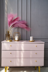 light pink dresser at the gray wall decorated with candles and colored feathers.